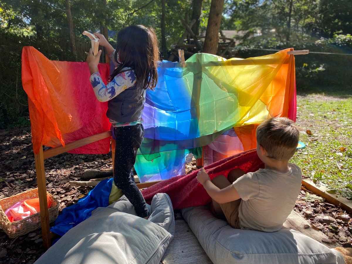 Children playing with rainbow silks outdoors at The Hilltop Playgarden